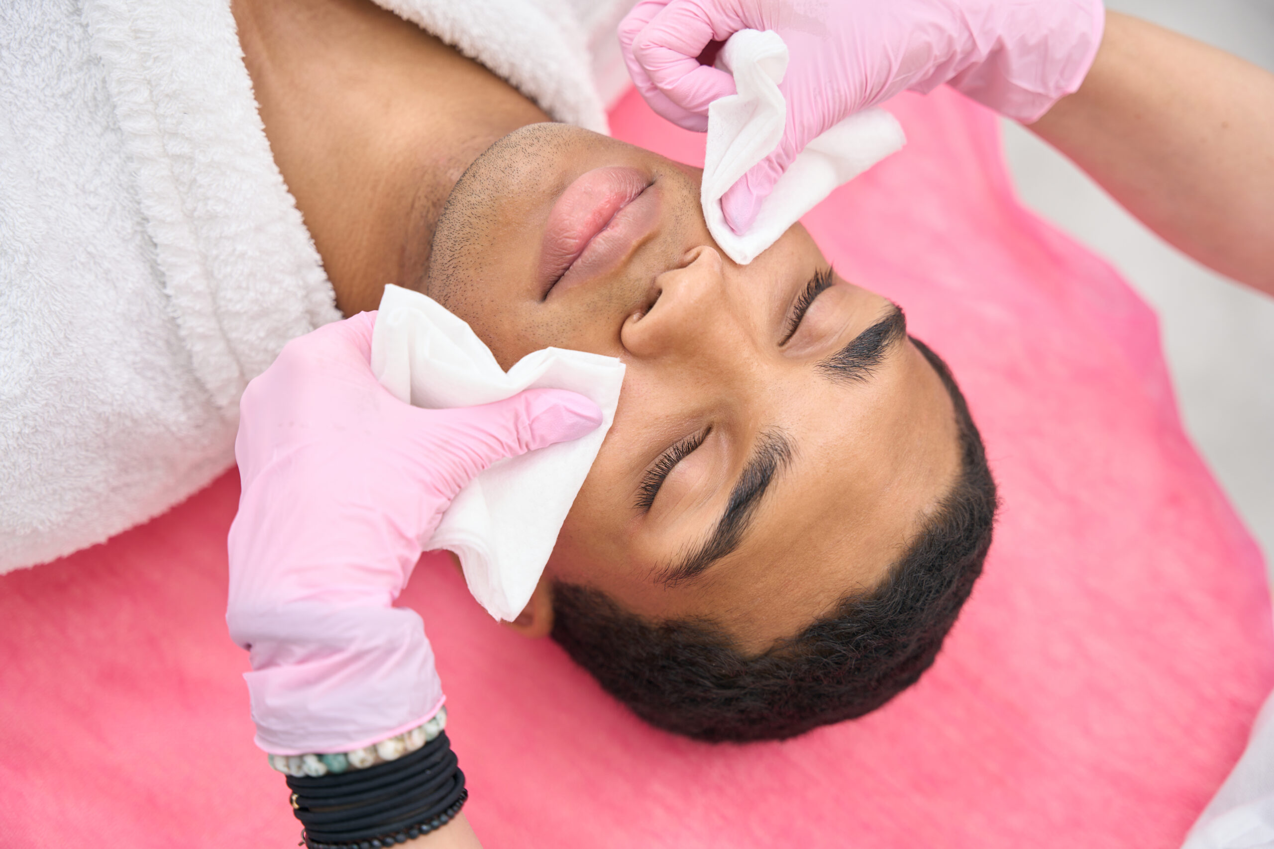 Doctor hands in nitrile gloves cleansing young man skin with wet disposable face towels